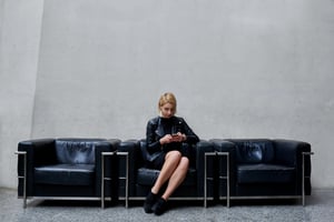 Mujer de traje alternativo y moderno sentada en un sofá negro observando su celular 