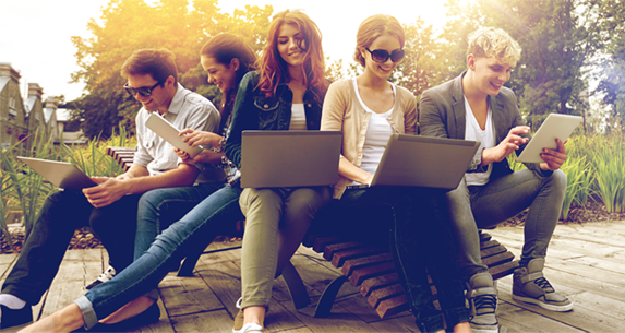 Cinco adolescentes sentados en una banca e interactuando con dispositivos electrónicos