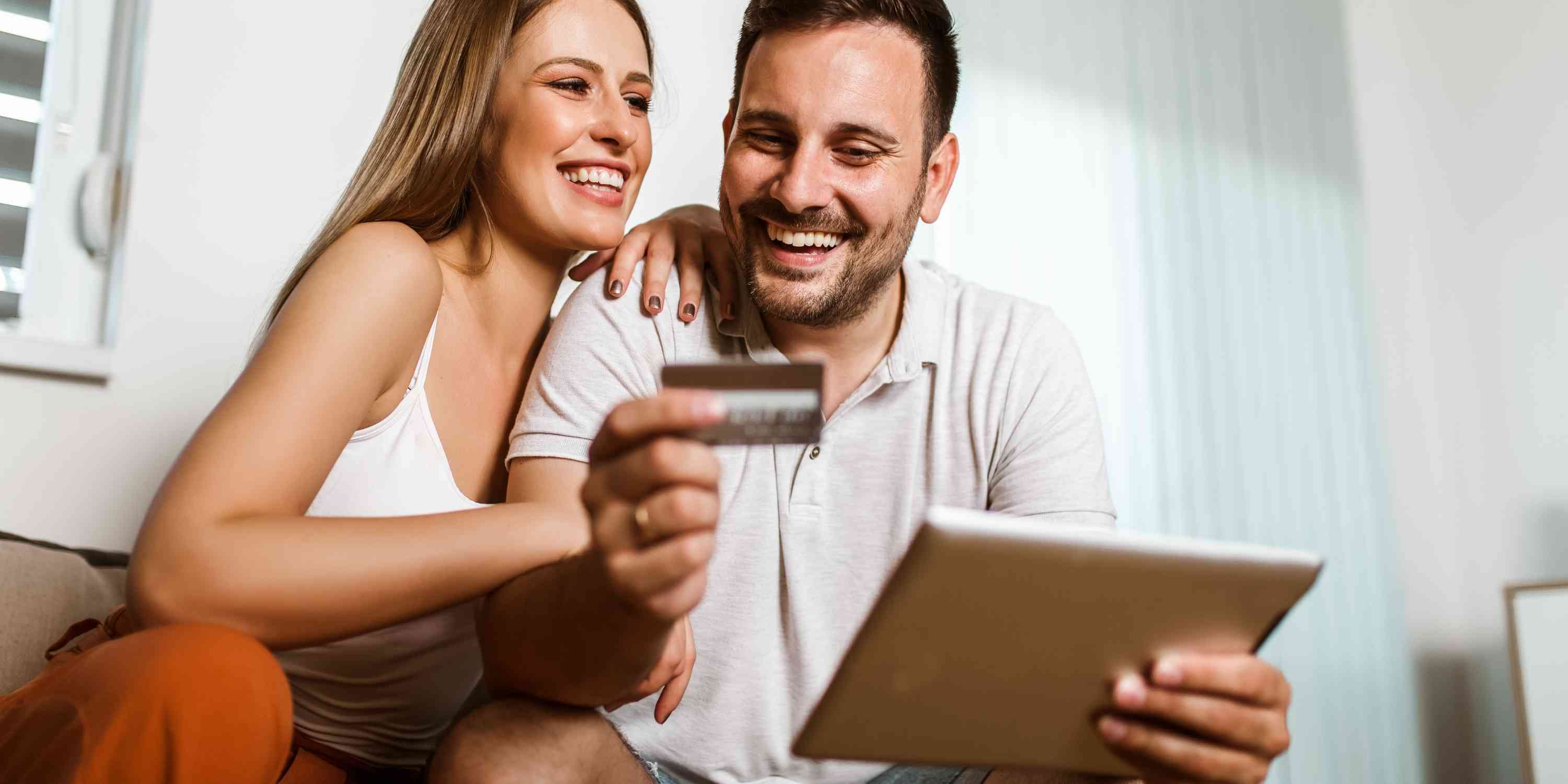 Happy couple hold credit card while using tablet